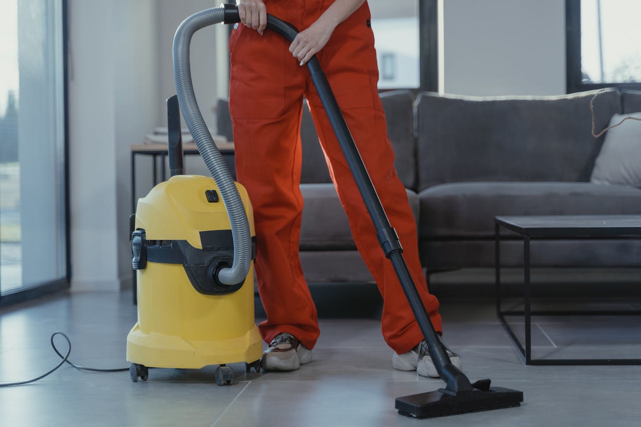 our-story A professional cleaner in red coveralls vacuums a contemporary living room with a yellow vacuum cleaner.